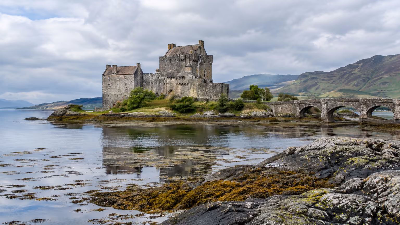 Eilean Donan Castle and its stone bridge viewed from the loch shore