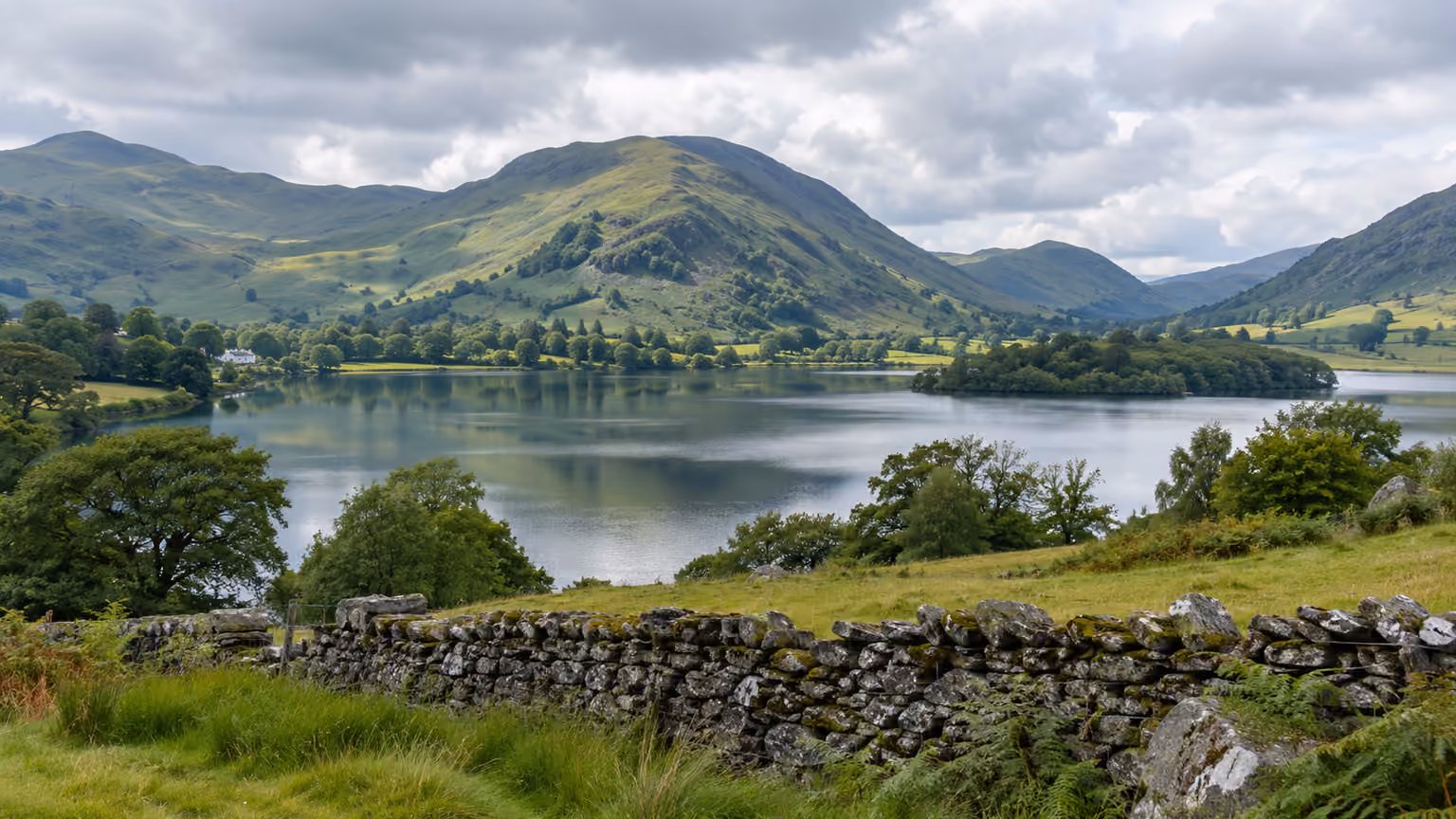 A quiet Lake District landscape in England with a calm lake below green rounded fells and a low
