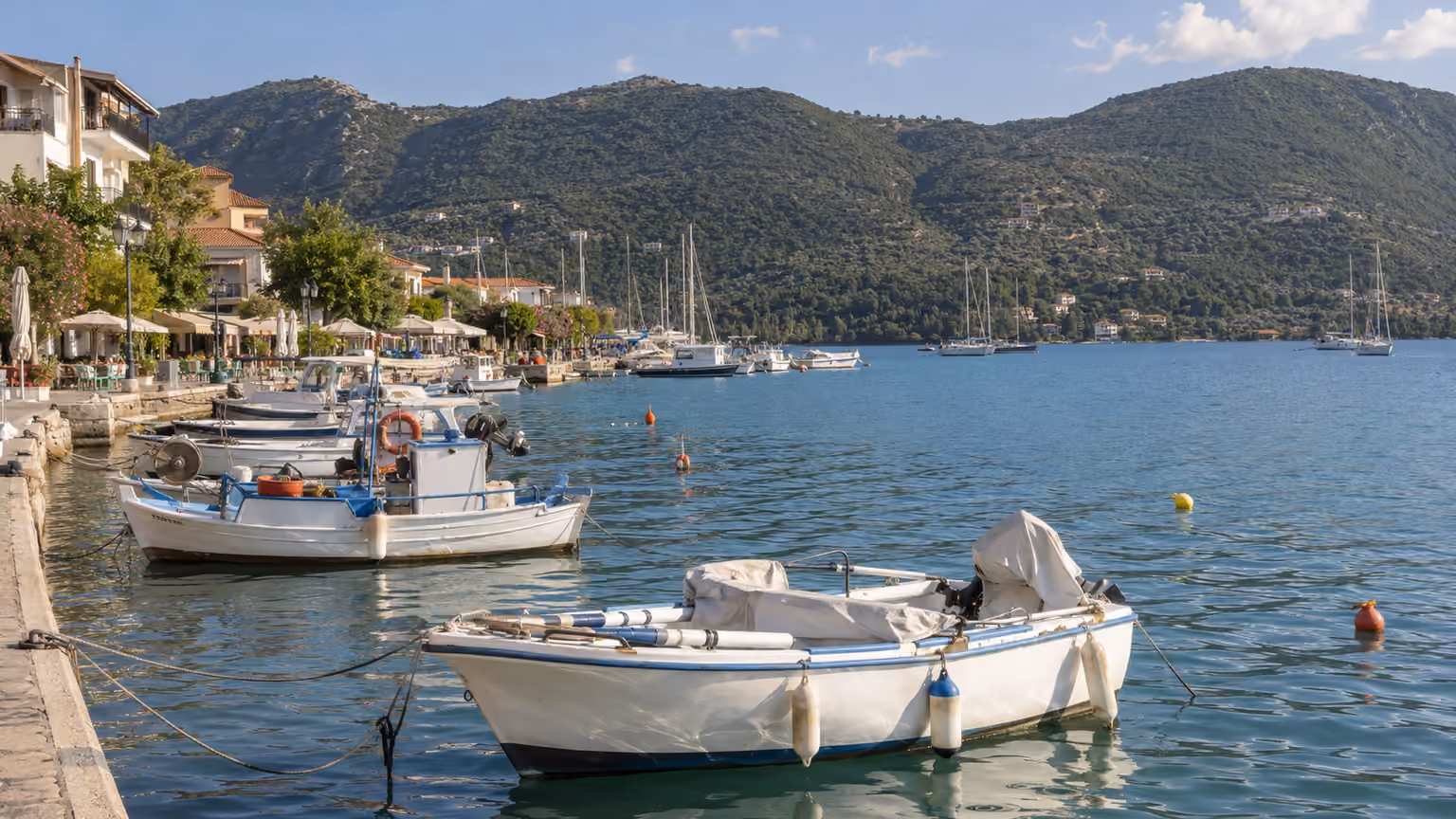The waterfront and small moored boats at Nidri on Lefkada Greece with green hills across the bay