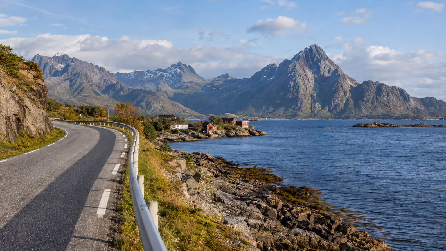 A quiet Lofoten coastal road curving beside cold blue water and low rocky shore