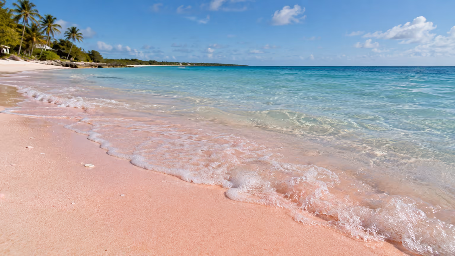 Small clear shore waves washing across subtly pink coral sand on Harbour Island Bahamas