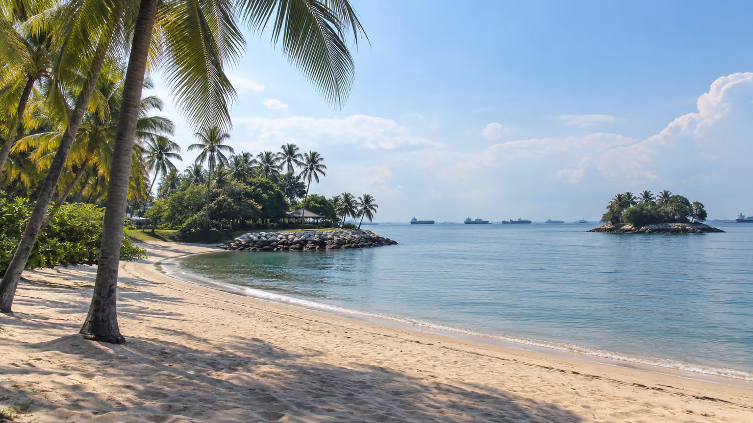 A quiet palm-fringed sandy beach on Sentosa Singapore with calm sea and tropical coastal