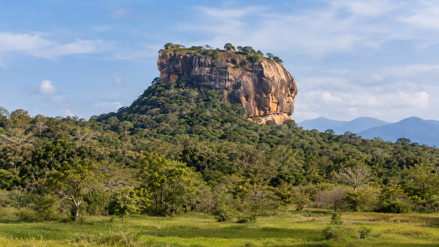 The rocky Sigiriya fortress outcrop rising beyond low green tropical woodland in Sri Lanka
