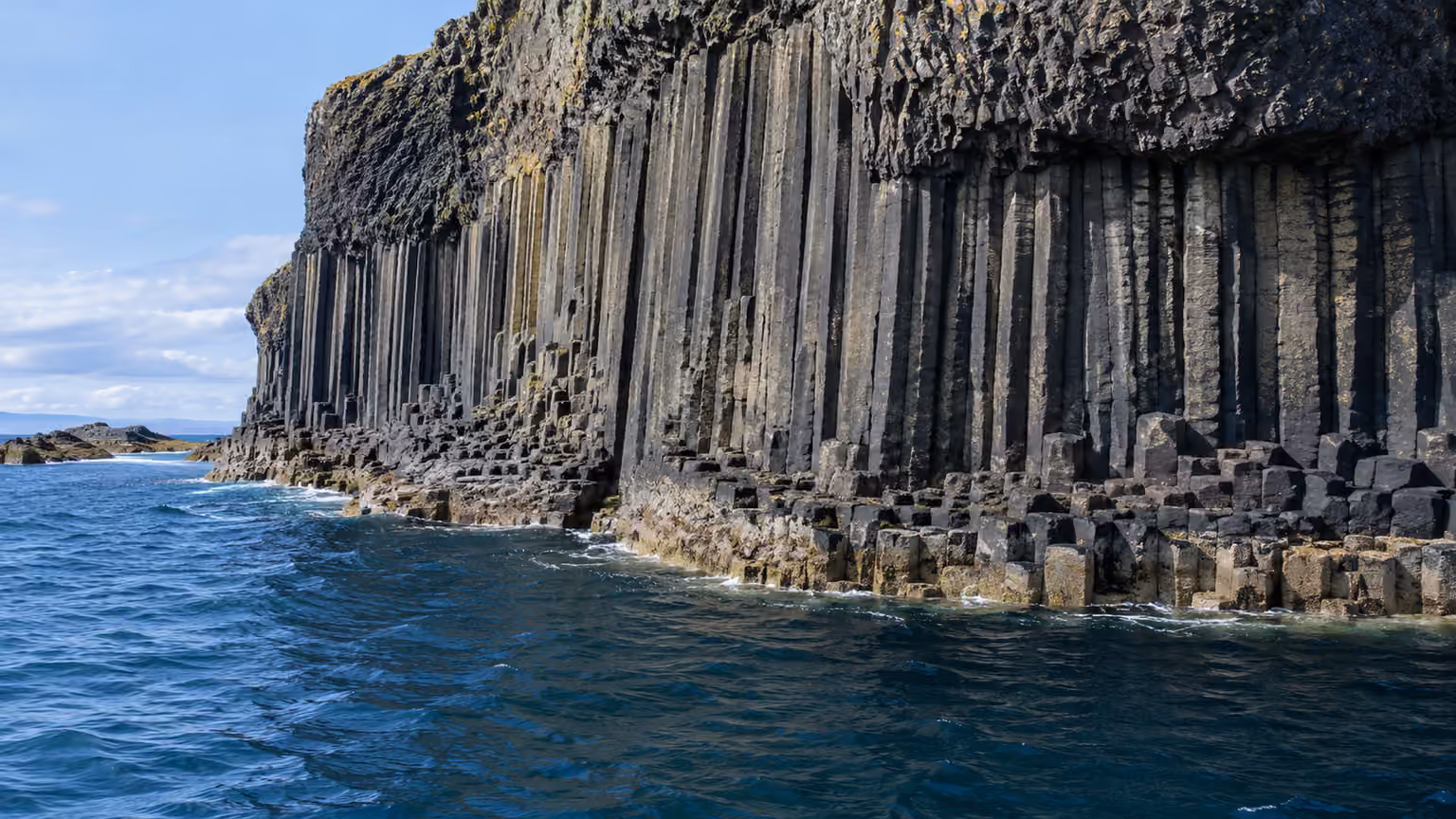 Close geological view of vertical hexagonal basalt columns along Staffa's shoreline with dark