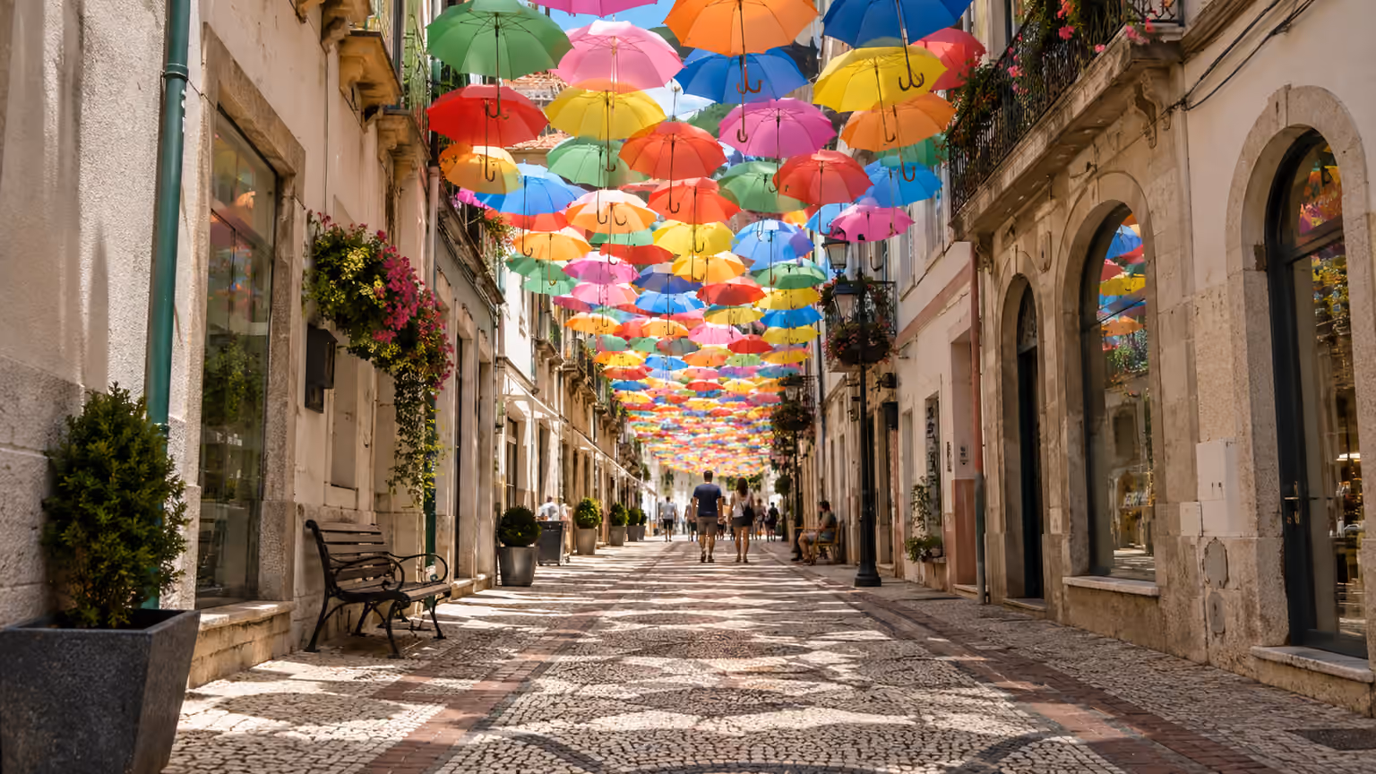 A ground-level view along a shaded Agueda street beneath colorful suspended umbrellas
