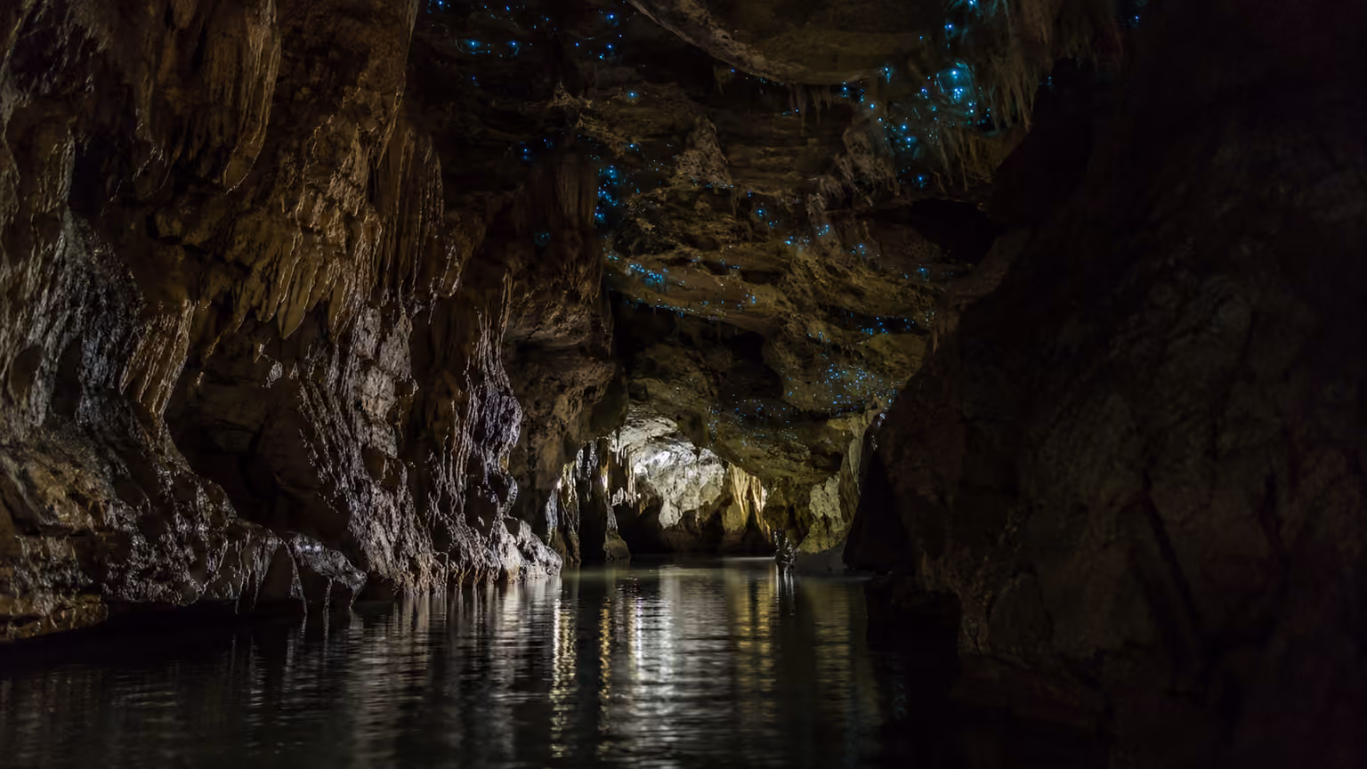 Waitomo limestone cave New Zealand with faint blue glowworms above a dark underground stream