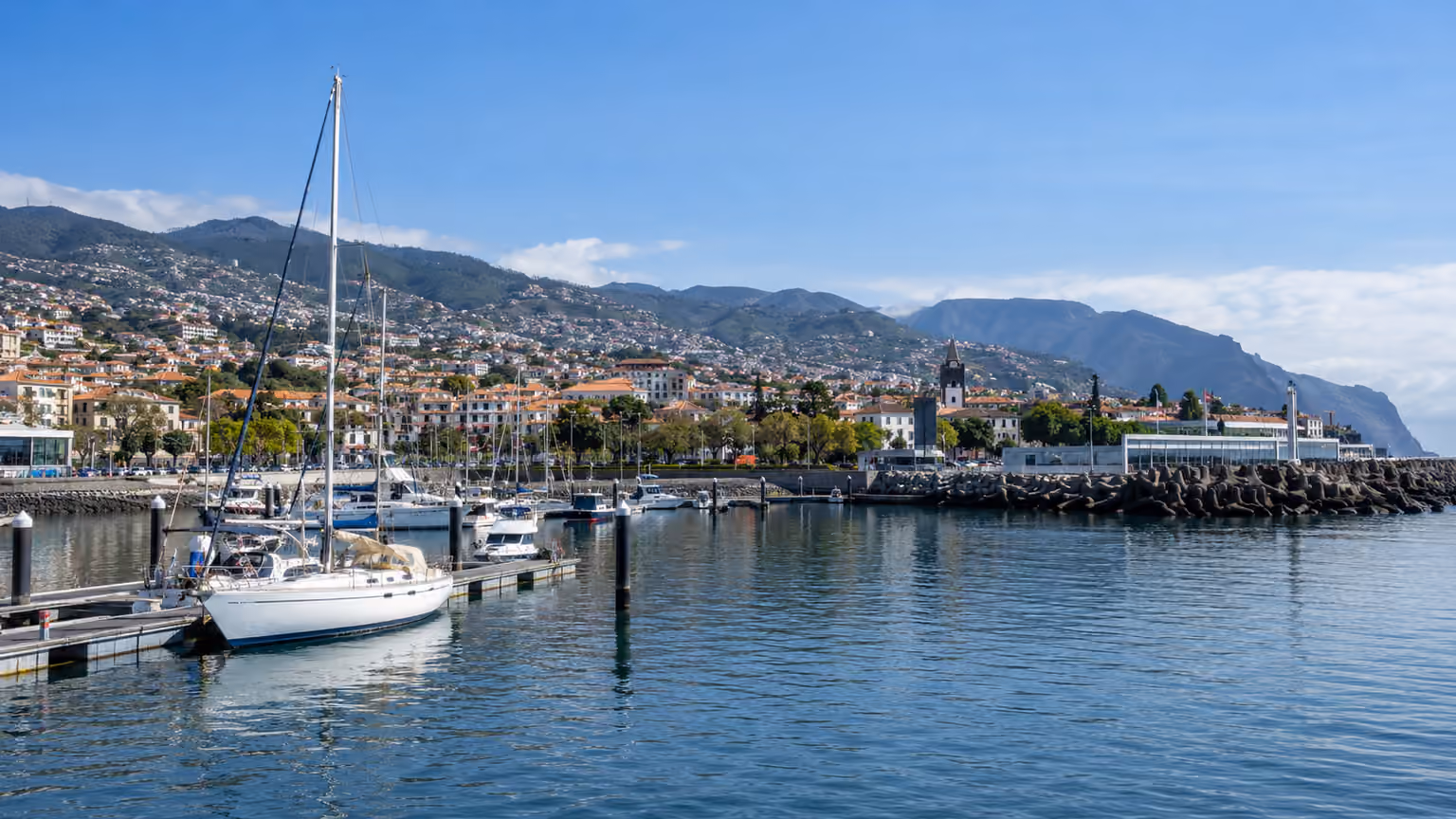 The Funchal marina and harbour on Madeira with sailing boats and distant terracotta-roofed