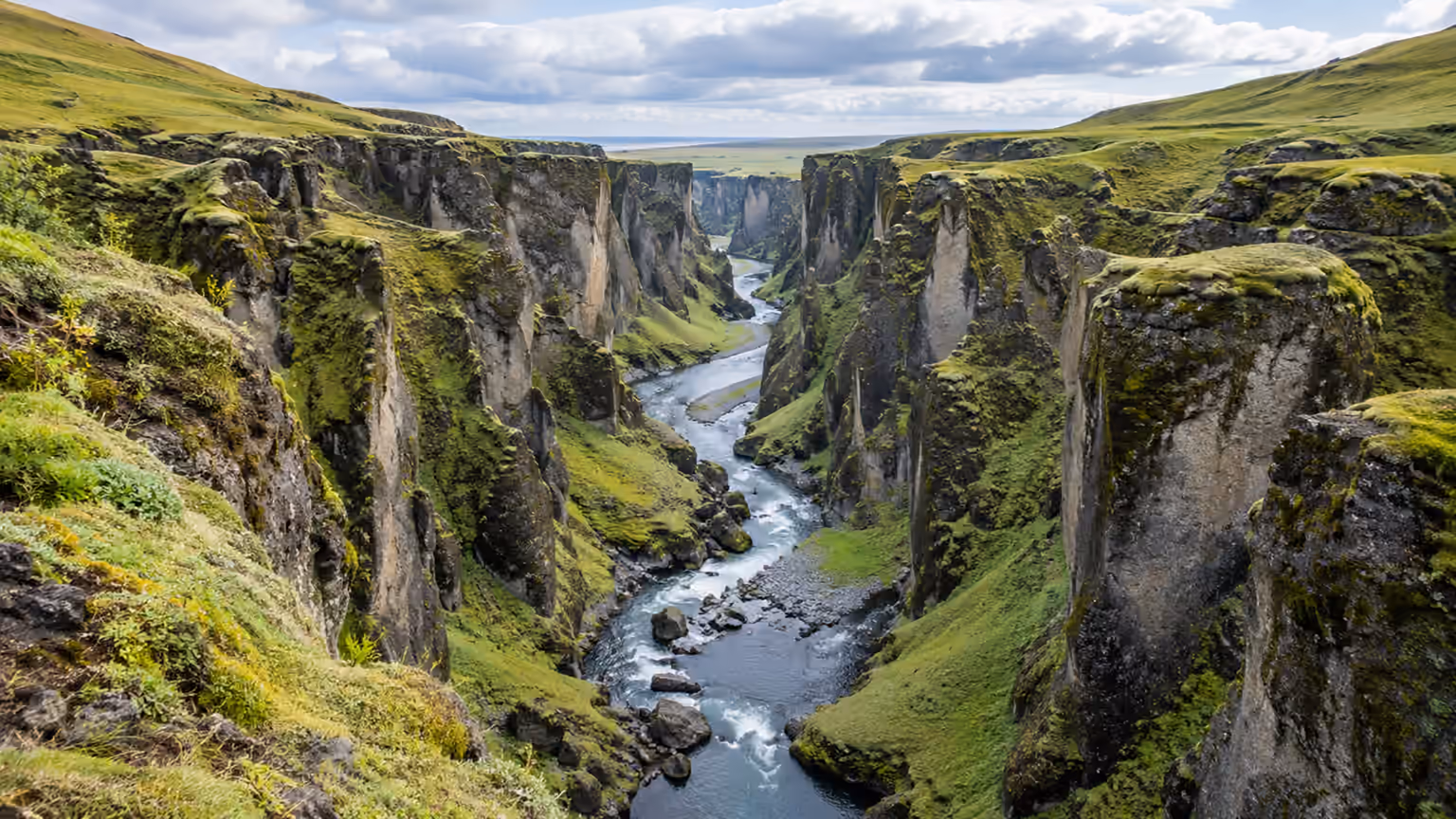 A winding river between steep moss-covered canyon walls under a cloudy sky