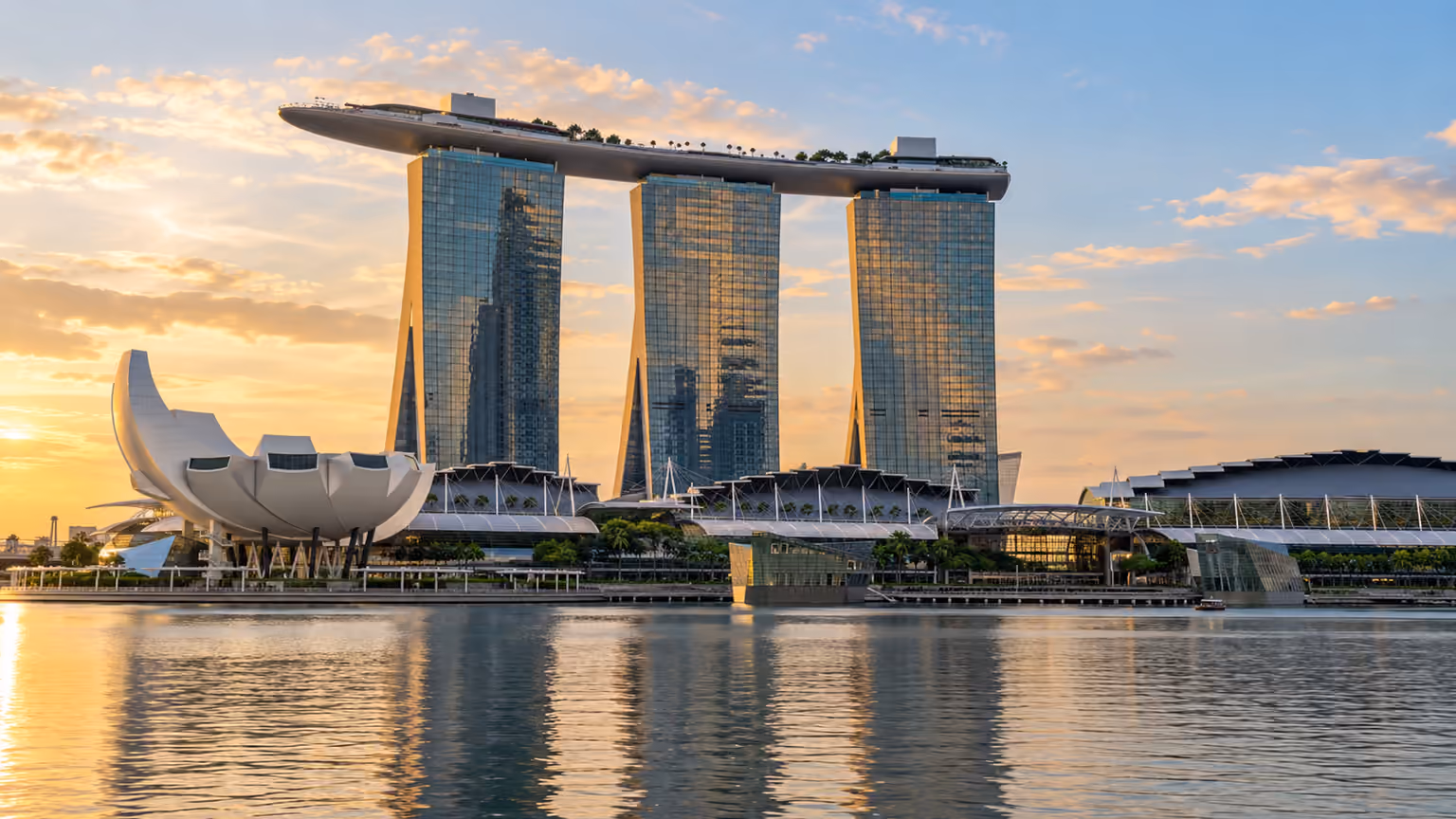 Three waterfront towers beneath a long rooftop skypark in warm evening light