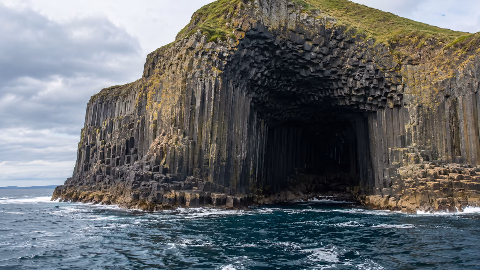 Dark basalt columns around a sea cave opening above Atlantic waves