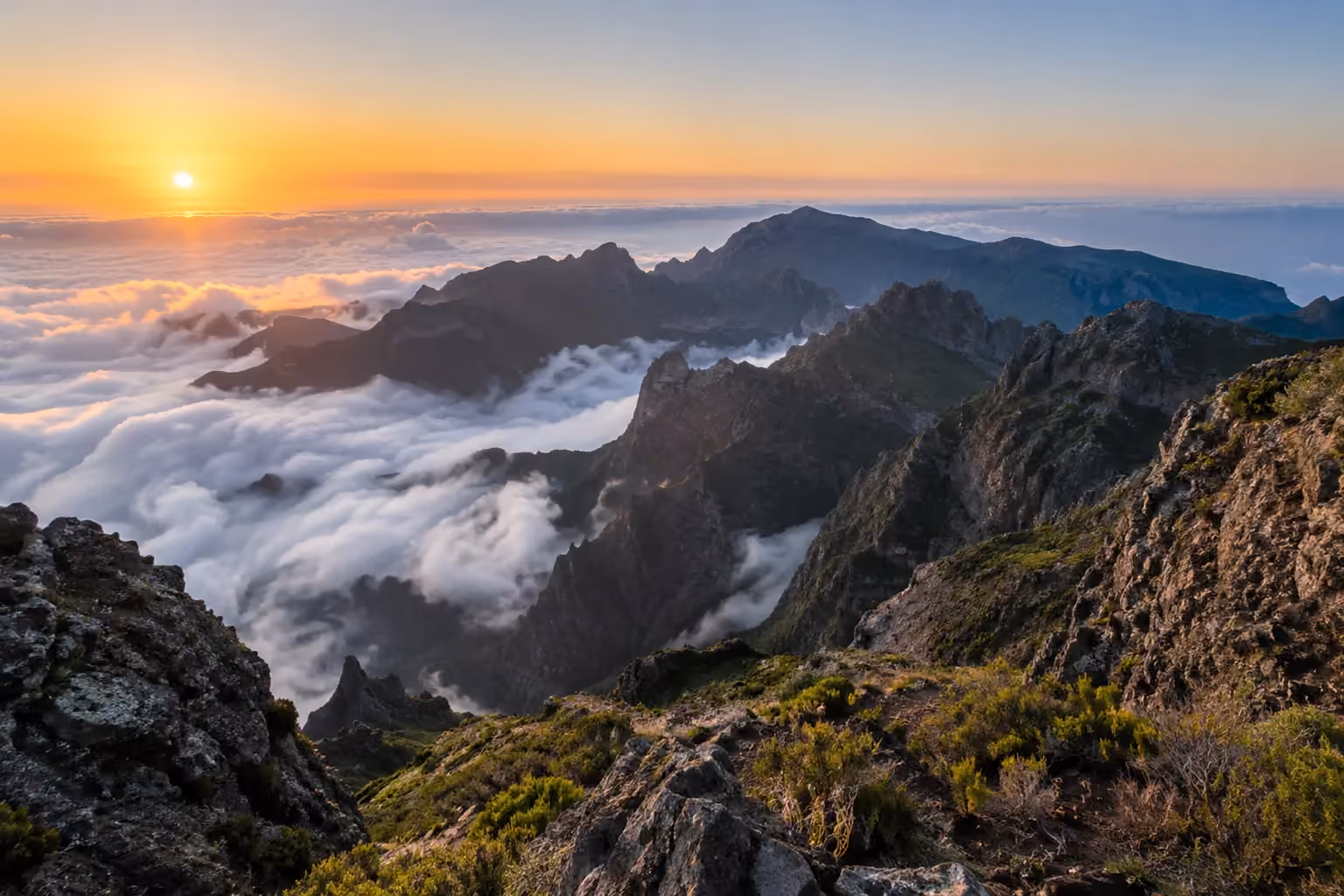 Jagged volcanic ridges with green vegetation above white clouds at sunrise