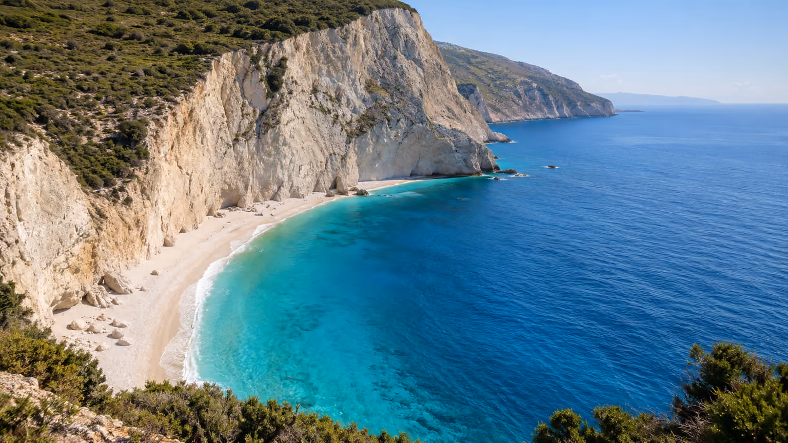 Pale beach below white limestone cliffs beside blue Ionian water on Lefkada