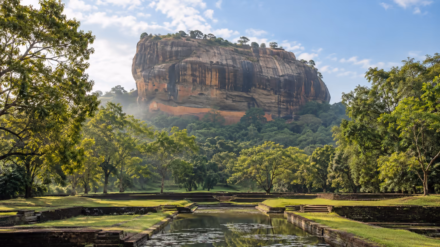 A flat-topped granite rock rising above green forest and garden pools in Sri Lanka