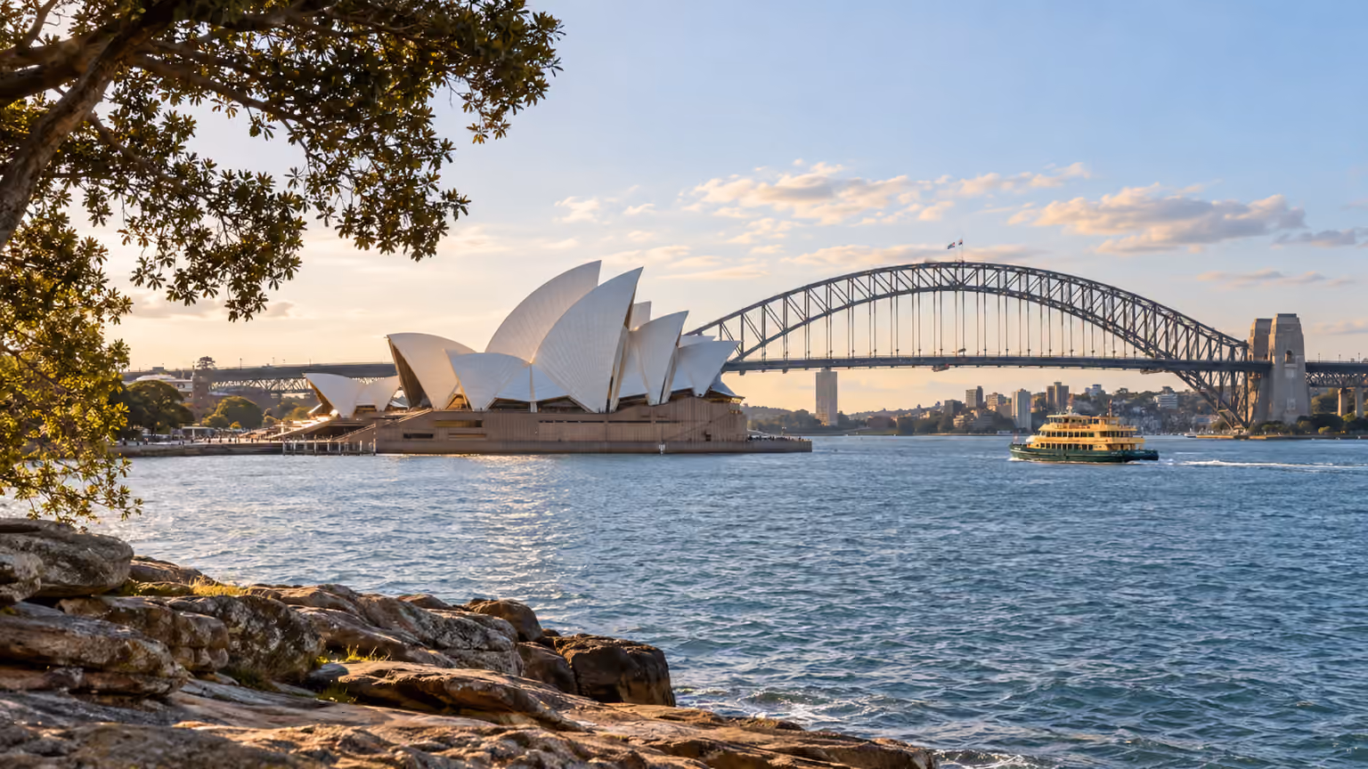 Sydney Opera House and Harbour Bridge across the water with a small ferry
