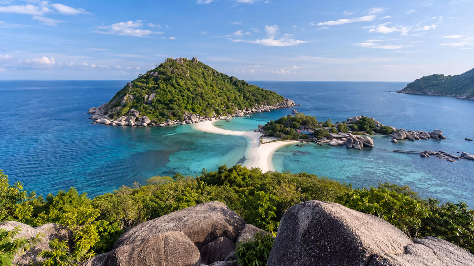 Green granite islets joined by a narrow white sandbar in turquoise tropical water