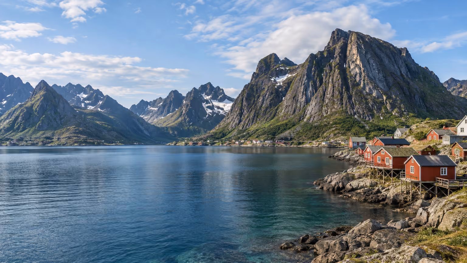 Red timber fishing cabins beside a fjord beneath steep northern Norwegian mountains