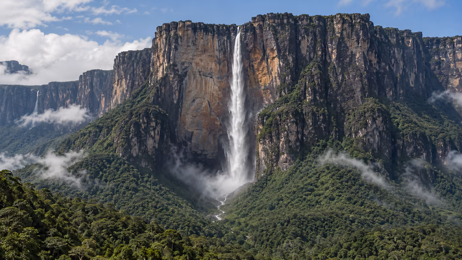 A tall narrow waterfall descending from a tepui cliff above misty Venezuelan rainforest