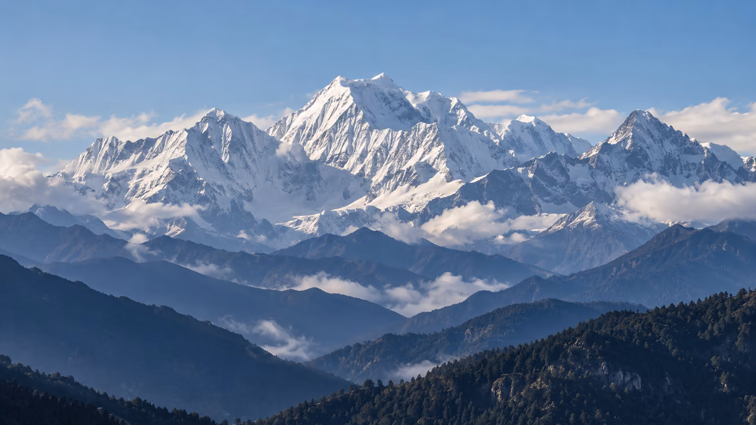 A remote snow-covered Himalayan summit above layered forested valleys in Bhutan