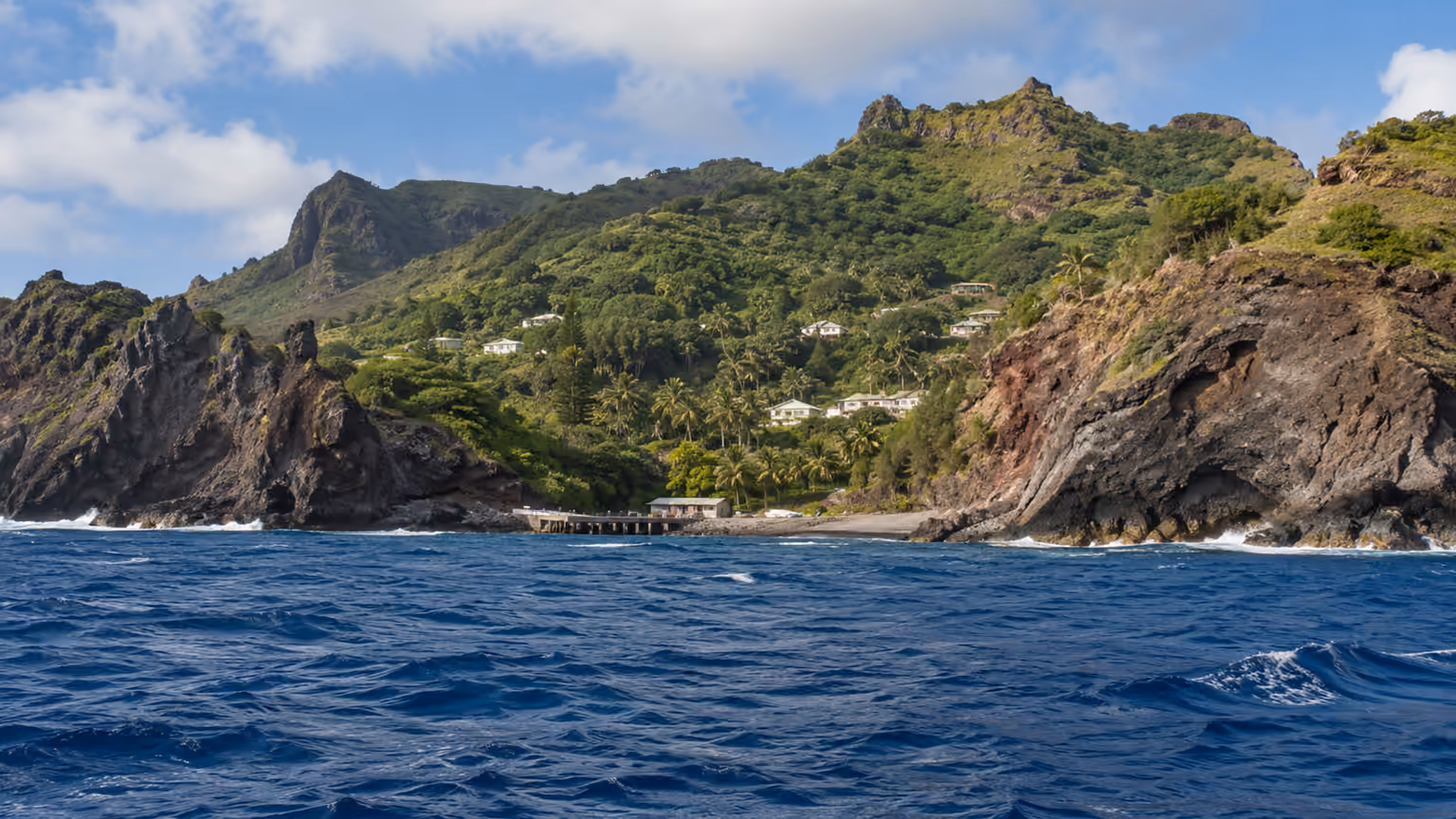 Green cliffs and a small coastal settlement above deep blue water on Pitcairn Island