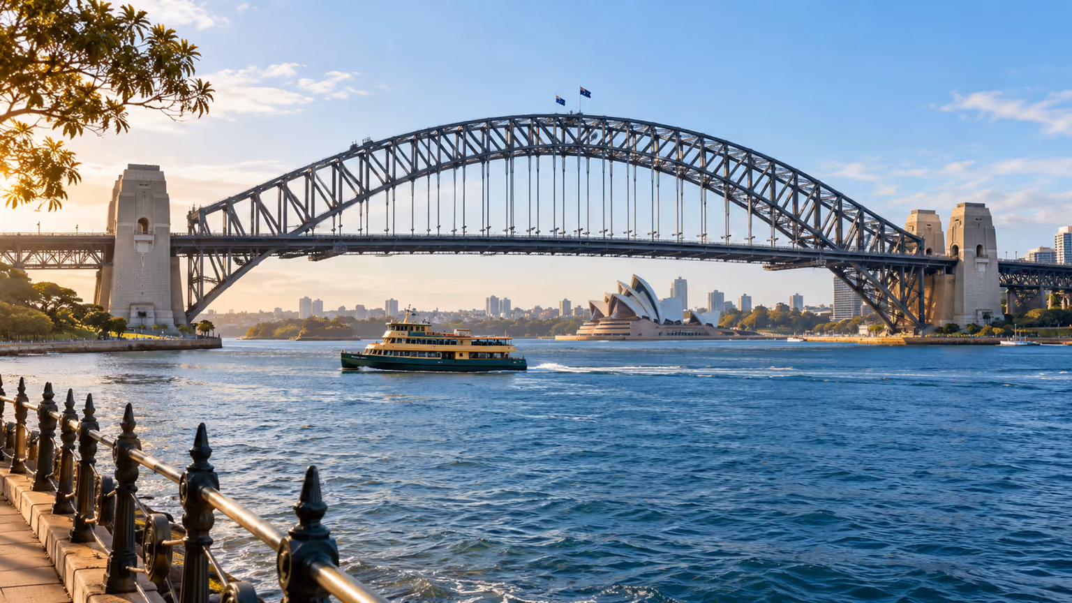 The steel arch of Sydney Harbour Bridge above blue water and the harbour foreshore